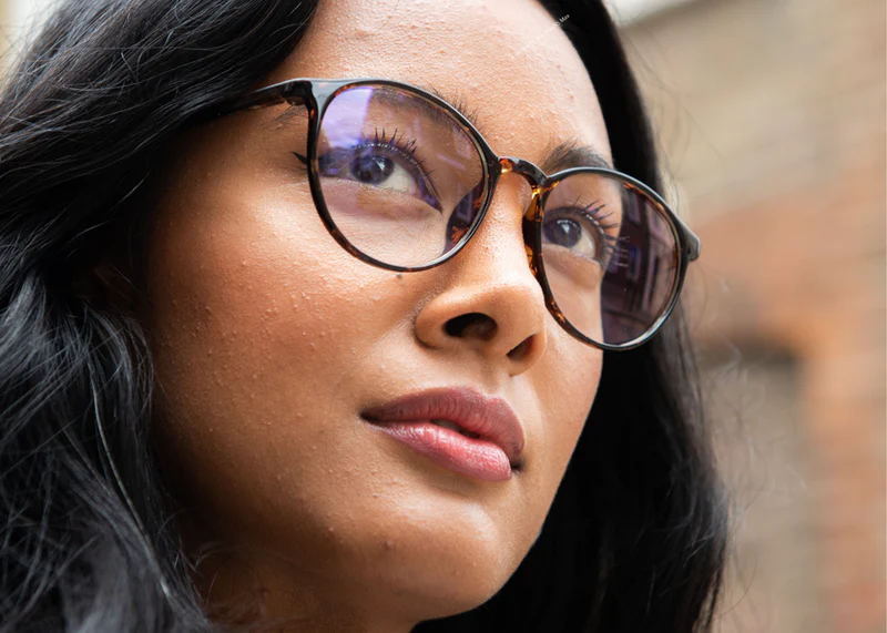 Woman wearing tortoiseshell Ocushield Clear All-Day Blue Light Glasses, looking upward in profile view against blurred background.