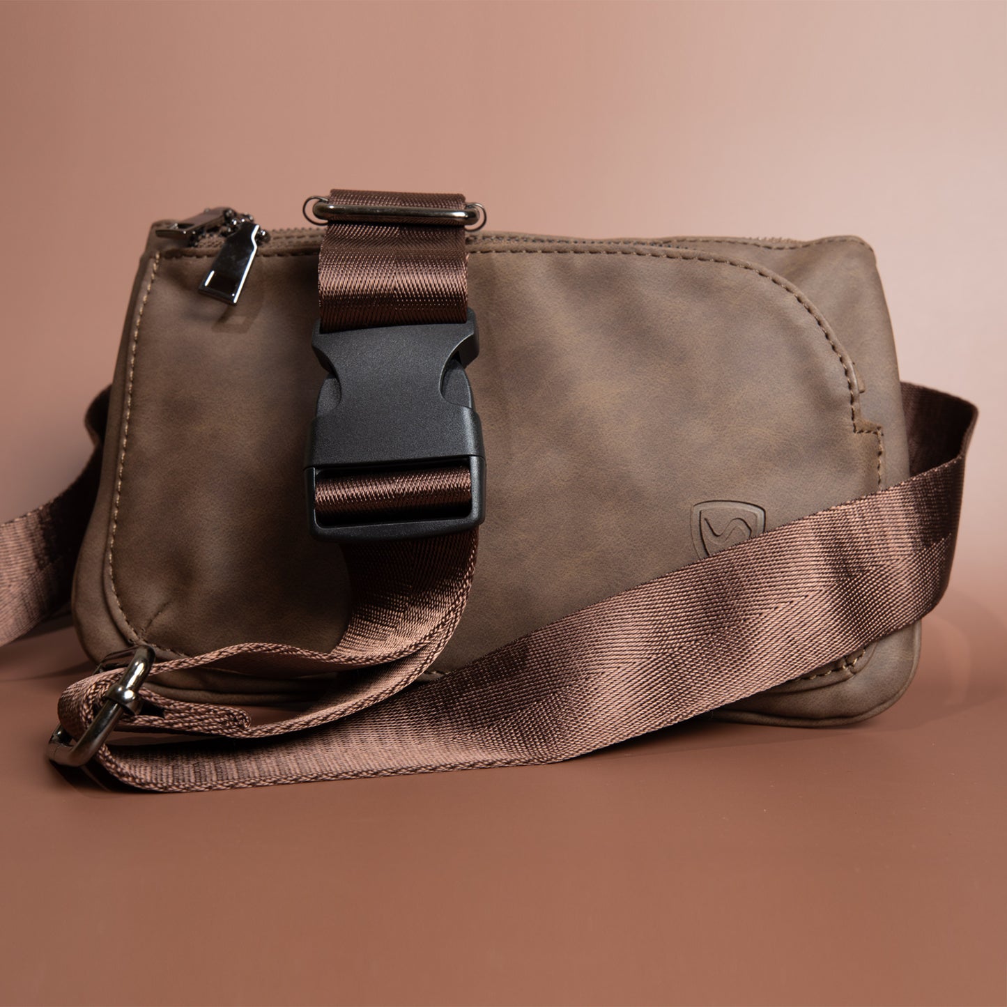 SYB Cross Body Fanny Pack in taupe vegan leather with brown strap and buckle closure, front view against tan background.