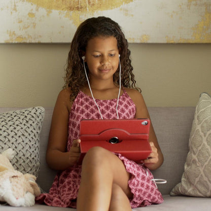 Girl using red SafeSleeve Universal Tablet Case while sitting on couch with earbuds in, case shown in use.