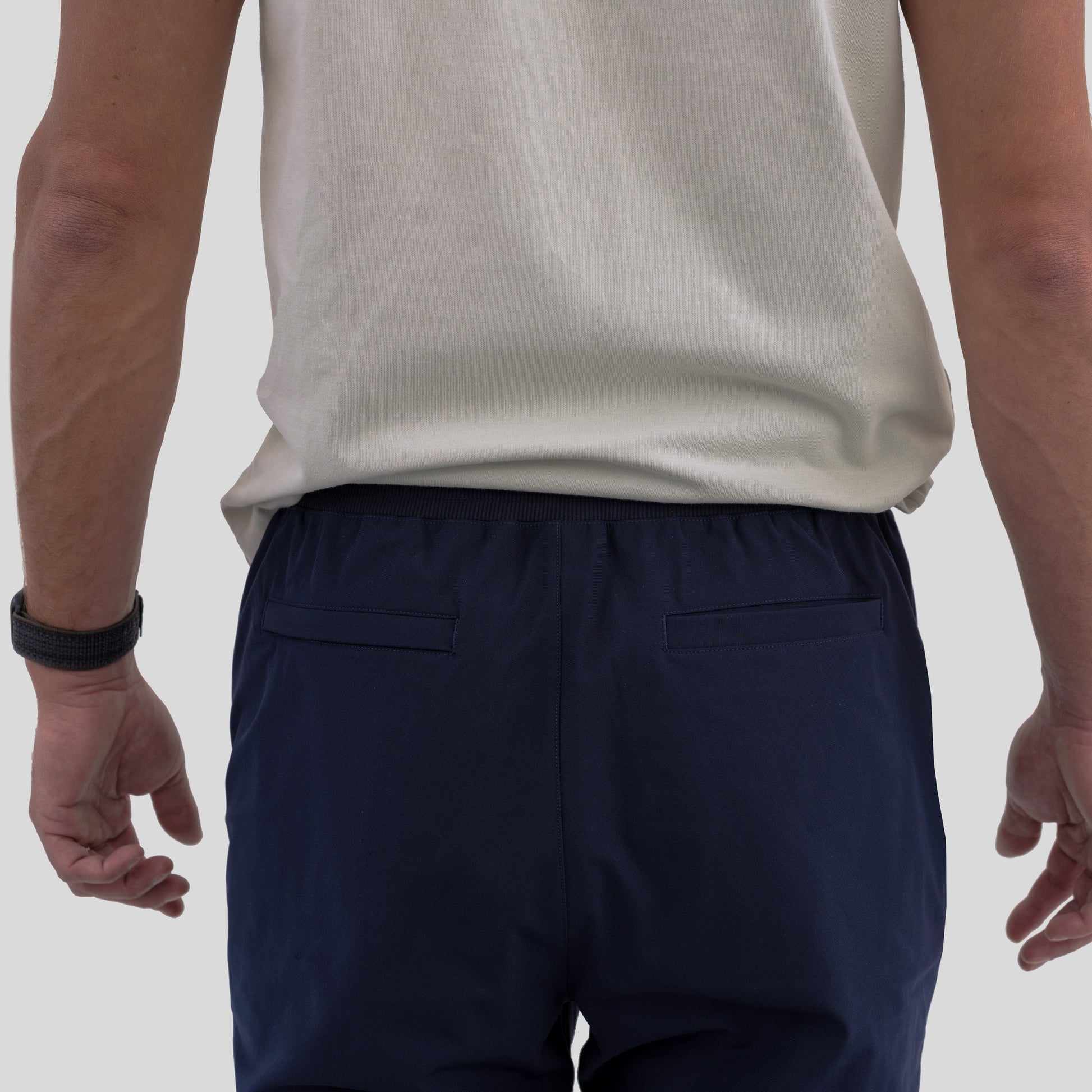 Back view of HAVN WaveStopper™ Joggers in navy, showing rear pockets and elastic waistband on male model wearing cream tank top.