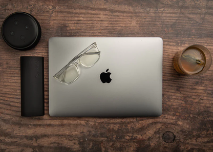 Ocushield Clear All-Day Blue Light Glasses displayed on MacBook with coffee and accessories on wooden desk.