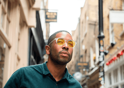 Man wearing amber-tinted Ocushield blue light glasses on urban street, looking upward.