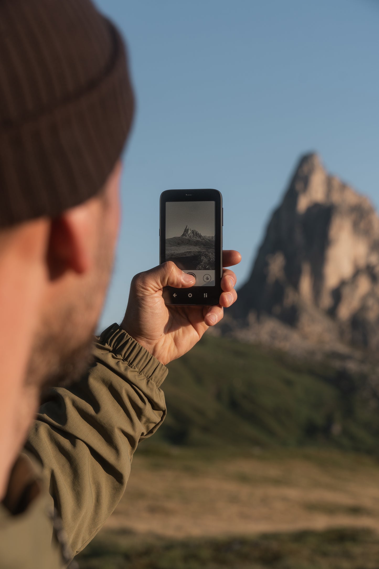 Person holding Mudita Kompakt phone capturing mountain landscape photo, demonstrating device in outdoor use.