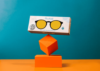 Ocushield Amber blue light blocking glasses displayed on stacked orange geometric blocks against turquoise background.