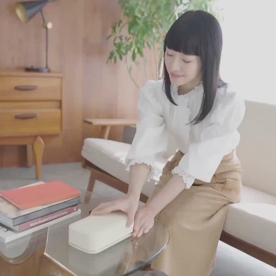 Marie Kondo setting the Bagby Stolp x KonMari Faraday phone box down on a coffee table beside a stack of books.