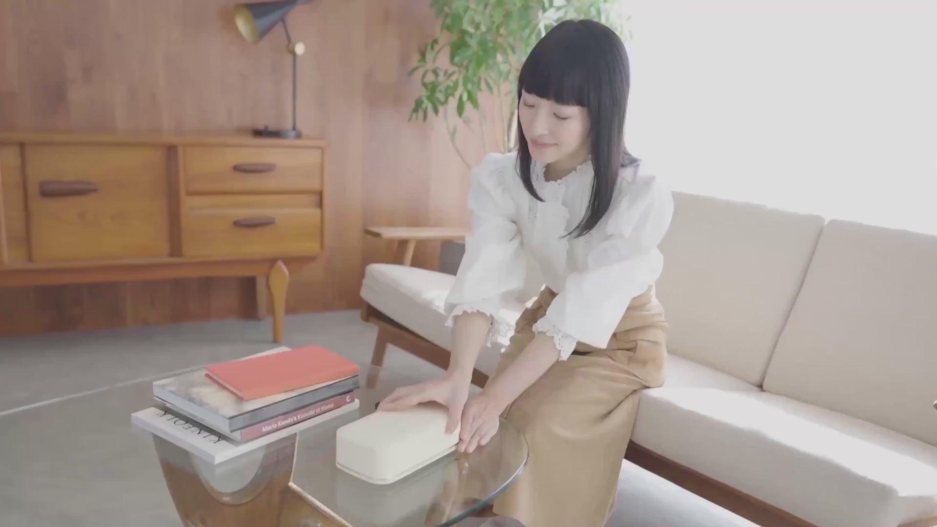Marie Kondo setting the Bagby Stolp x KonMari Faraday phone box down on a coffee table beside a stack of books.