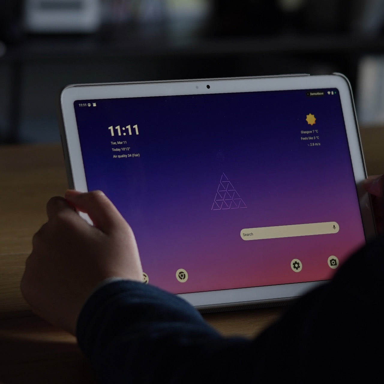 Child's hand holding white tablet displaying purple gradient home screen with time 11:11, weather info, and search bar.