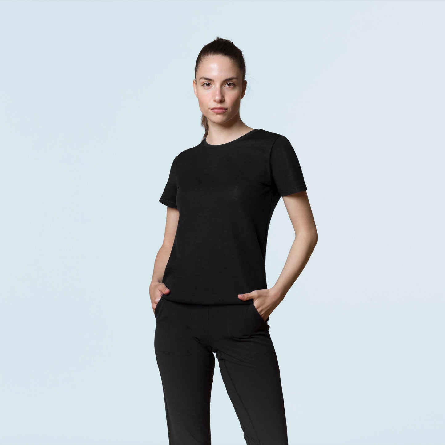 Woman wearing black HAVN WaveStopper™ T-Shirt 2.0 and black pants, standing against light blue background, front view.