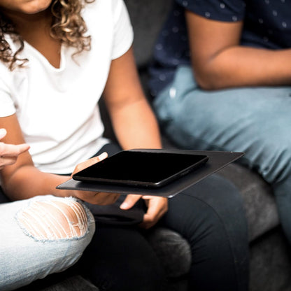 Two people sitting together holding a black SYB Tablet Pad with a smartphone on top, demonstrating the product in use.