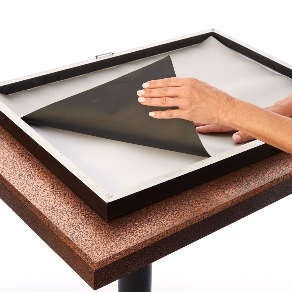 Hand peeling back black SYB Poster Frame Liner to reveal white surface underneath on wooden table.
