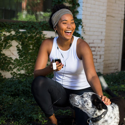 Woman wearing SYB H.A.R.D. headset device while exercising outdoors with dog, smiling.
