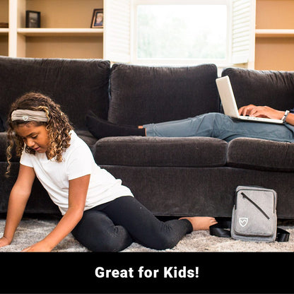 Child sitting on floor near couch with SYB Sling Bag beside her, adult using laptop in background.