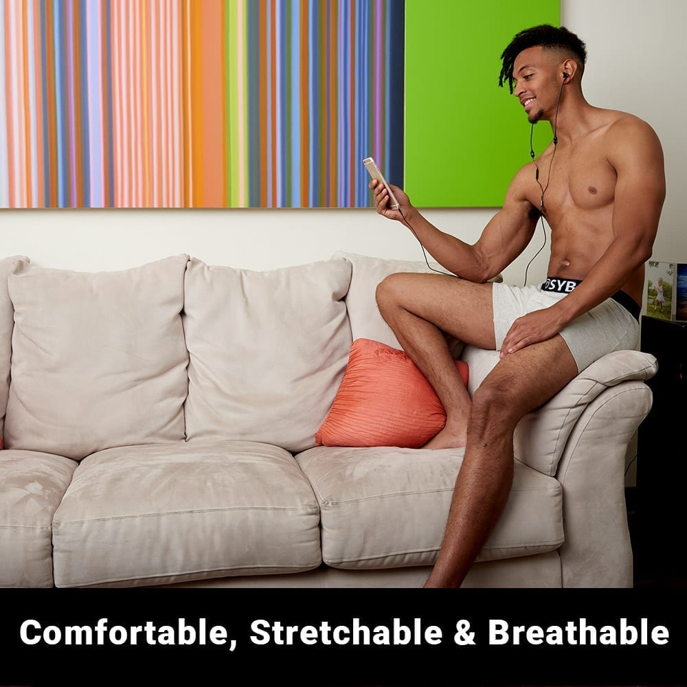 Man wearing white SYB Boxer Briefs sitting on beige couch, holding phone, demonstrating comfort and stretchability of the garment.