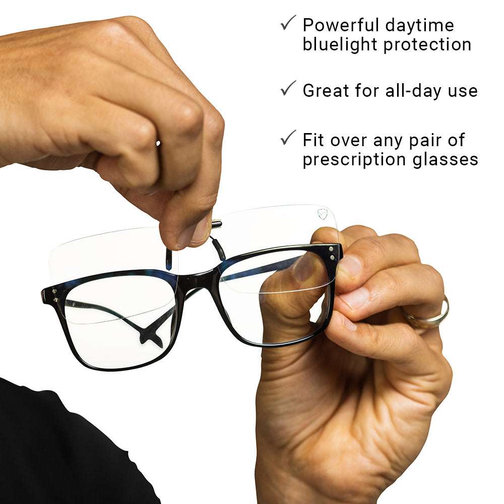 Hands demonstrating SYB Clip-On Bluelight Glasses fitted over black prescription frames, with key features listed: daytime bluelight protection, all-day use, and universal fit.