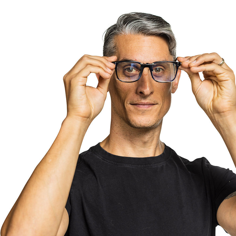 Man wearing black SYB Clip-On Bluelight Glasses with dark frames, adjusting them with both hands against white background.