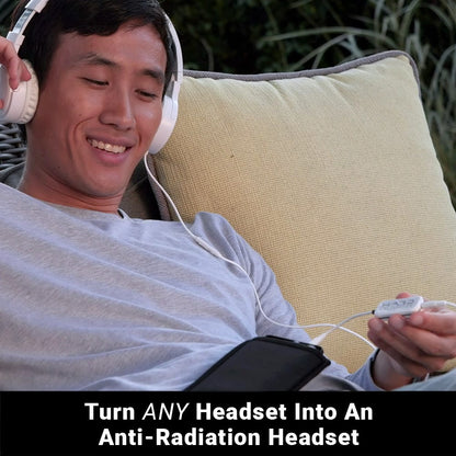 Man wearing white headphones and SYB H.A.R.D. device while holding mobile phone outdoors, smiling.