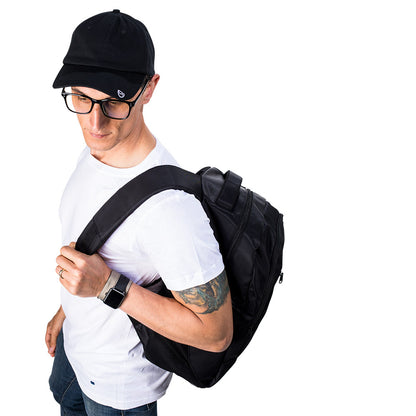 Man wearing black SYB backpack over white shirt, shown from side angle with backpack straps visible and smartwatch on wrist.