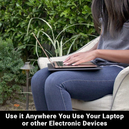Woman using SYB Laptop Pad on her lap while sitting in chair outdoors surrounded by green plants and foliage.