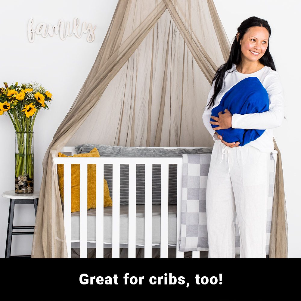Pregnant woman holding blue pillow next to white crib with SYB Faraday Serenity Canopy draped overhead in nursery setting.