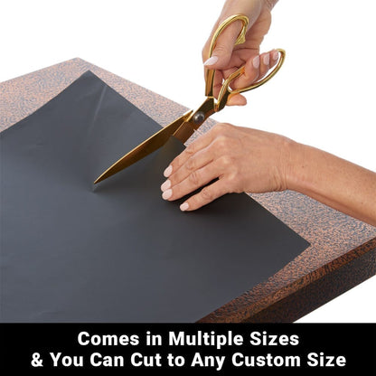 Scissors cutting dark SYB Poster Frame Liner material on cork-backed surface, demonstrating custom sizing capability.