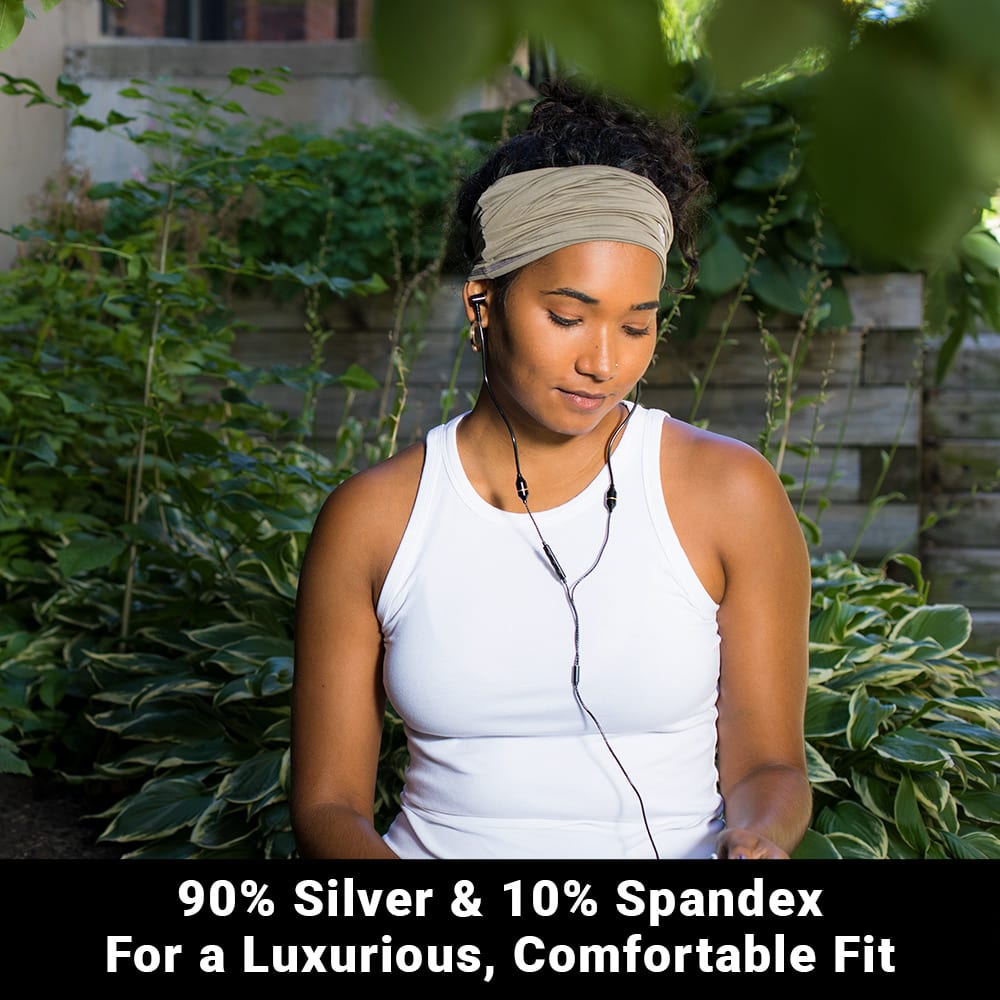 Woman wearing white SYB Neck Gaiter as headband in garden setting, showing fabric composition of 90% silver and 10% spandex.